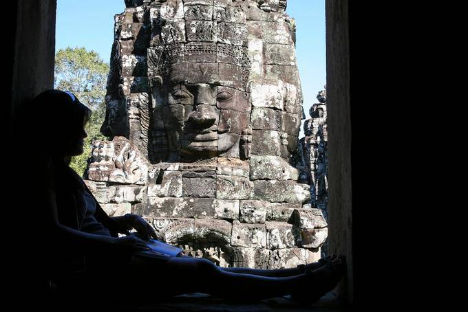 Reading in the shade in front of the stone face, Bayon, Angkor Thom, Angkor, Cambodia