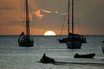 Deshaies, half sun setting between boats in silhouette, Guadeloupe.