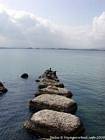 Fishermen on the pier in black volcanic stones, Syracuse, Sicily, Italy.