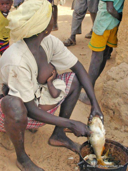 Woman feeding her child while flaking fish - Region Mbam - Senegal